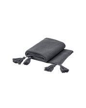 La Frazada de Lujo Chai Gris Oxford de Intima Hogar, de textura suave y borlas en las esquinas, se muestra doblada sobre fondo blanco; perfecta para añadir confort y estilo al hogar.