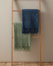 A wooden ladder displays Intima Hogar’s Frazada de Lujo Matcha Verde—a luxurious, fringed green throw—draped stylishly over a rung to elevate any neutral-walled, wooden-floored space with decoración de interiores.