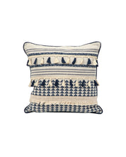 La funda de cojín Meknes de Intima Hogar presenta fondo crema, patrones geométricos azul marino y crema, filas texturizadas y borlas decorativas. Inspirada en la decoración marroquí, aporta un toque boho moderno a tu hogar.