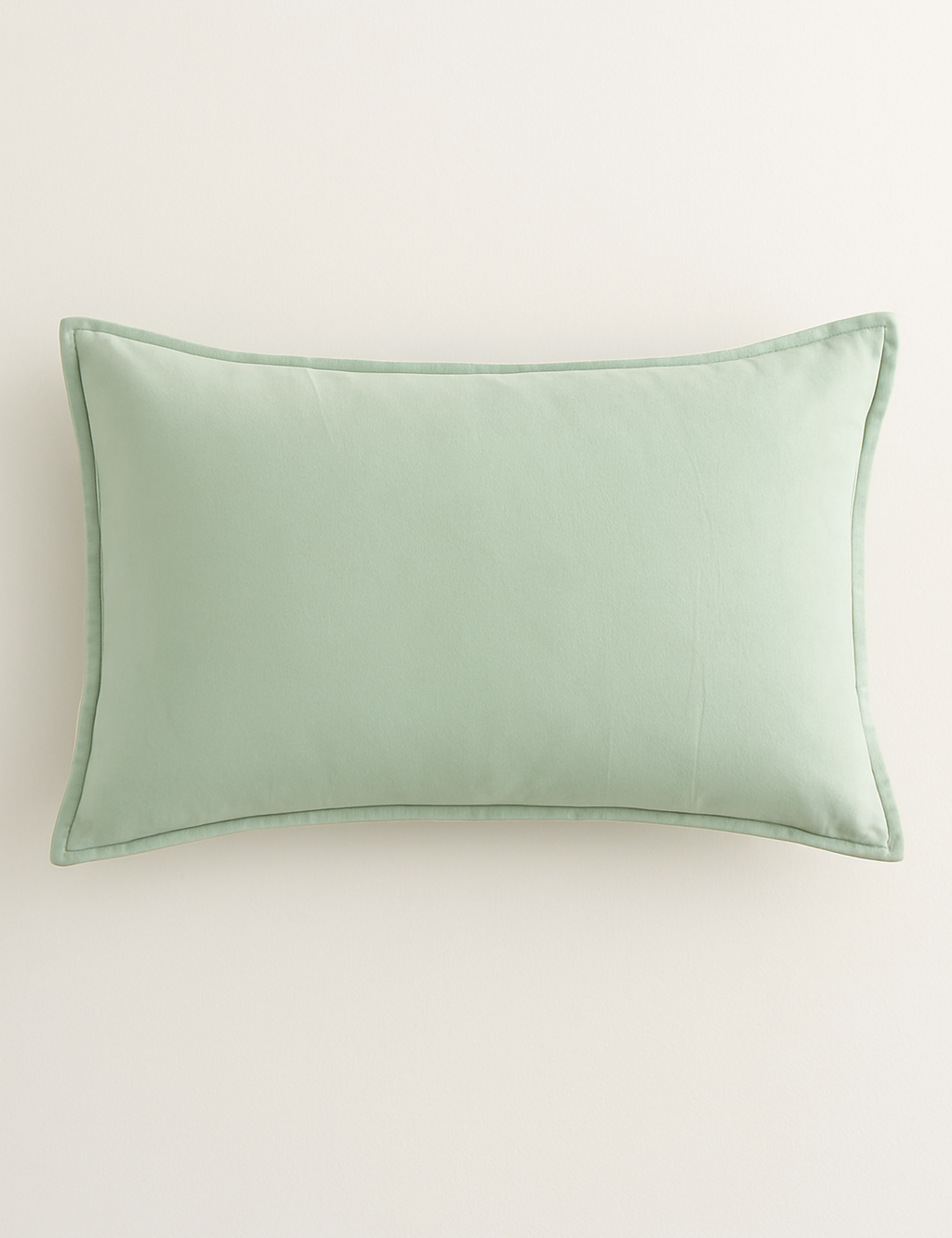 The Funda de Almohada Ensueño Verde Pistacho de Intima Hogar es una funda rectangular color verde pistacho, con textura suave y detalles sencillos, ideal para la cama o el descanso sobre un fondo blanco.