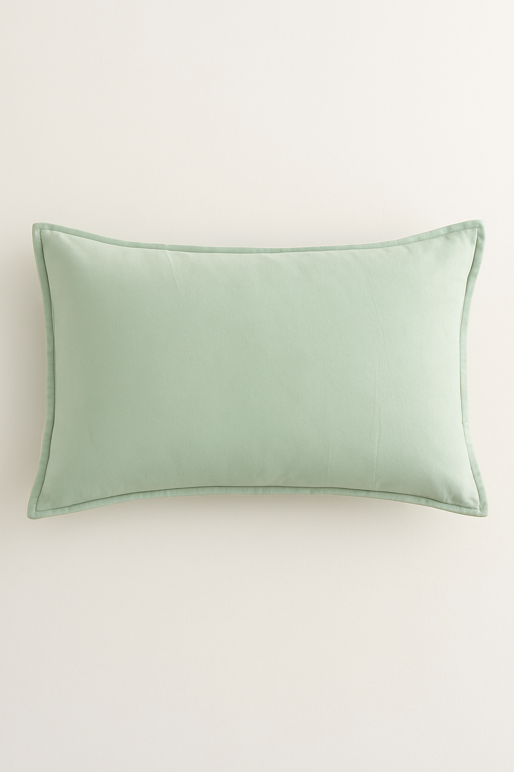 The Funda de Almohada Ensueño Verde Pistacho de Intima Hogar es una funda rectangular color verde pistacho, con textura suave y detalles sencillos, ideal para la cama o el descanso sobre un fondo blanco.