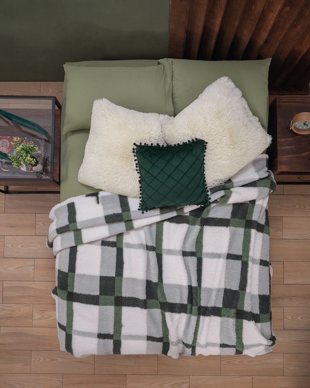 A neatly made bed features the Cojín de Lujo Velvet Verde Esmeralda by Intima Hogar and a green, white, and gray plaid blanket, with wooden nightstands on a light wood floor for an elegant touch.
