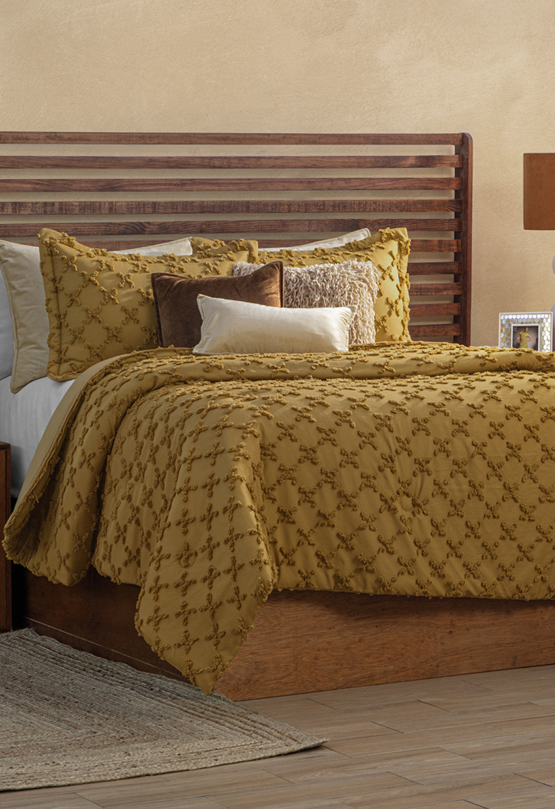 A neatly made bed with a wooden headboard features the Juego de Edredón Curry by Intima Hogar and decorative pillows in gold, white, and brown, all set on a wooden frame in a warm, neutral-toned room.