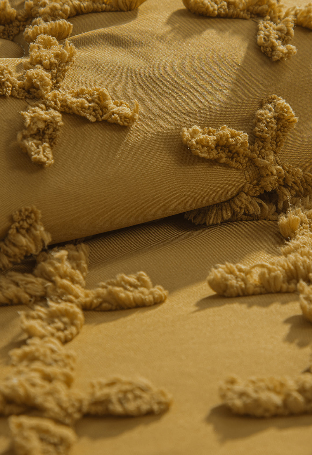 Close-up of the Juego de Edredón Curry by Intima Hogar: mustard yellow fabric with tufted X-shaped patterns, creating a cozy, plush, three-dimensional surface that adds warmth and texture to your space.