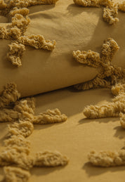 Close-up of the Juego de Edredón Curry by Intima Hogar: mustard yellow fabric with tufted X-shaped patterns, creating a cozy, plush, three-dimensional surface that adds warmth and texture to your space.