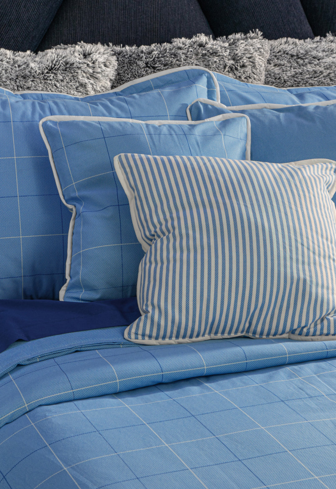 A neatly made bed featuring the Juego de Edredón Royal Cotton Eleganza by Intima Hogar, with blue checkered bedding and gray decorative pillows, creates a masculine look with timeless diseño clásico.