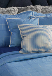 A neatly made bed featuring the Juego de Edredón Royal Cotton Eleganza by Intima Hogar, with blue checkered bedding and gray decorative pillows, creates a masculine look with timeless diseño clásico.