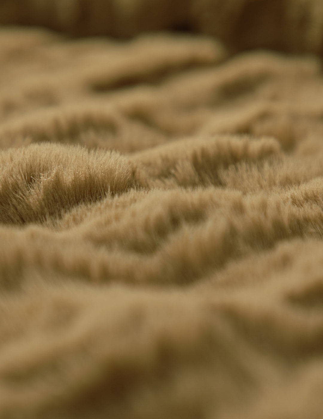 Close-up of the soft, light brown, fluffy surface of the Frazada de Lujo Quebec by Intima Hogar, featuring gentle waves and a textura esponjosa that resembles fur or a cozy blanket.