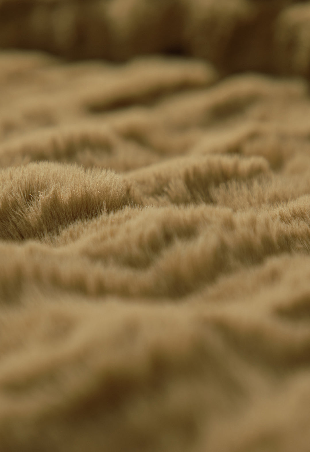 Close-up of the soft, light brown, fluffy surface of the Frazada de Lujo Quebec by Intima Hogar, featuring gentle waves and a textura esponjosa that resembles fur or a cozy blanket.