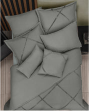 A neatly made cama minimalista features the Juego de Edredón Duvet Hamburgo de Intima Hogar, with grey bedding, an edredón blanco, and pillows with subtle dark crisscross lines, next to a wooden headboard and side table.