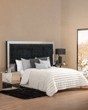 Modern bedroom featuring the Cobertor Platinum Extra Suave Antártida by Intima Hogar, white textured bedding, black headboard, gray and white accent pillows, mirrored nightstands, black lamp, framed photo, and a snowy window view.