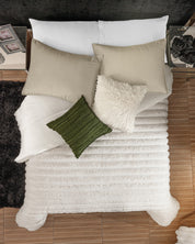 Top view of a bed made with the Cobertor Platinum Extra Suave Antártida by Intima Hogar, featuring beige and green pillows, a fluffy white pillow, nightstands, a black rug, and framed photos.
