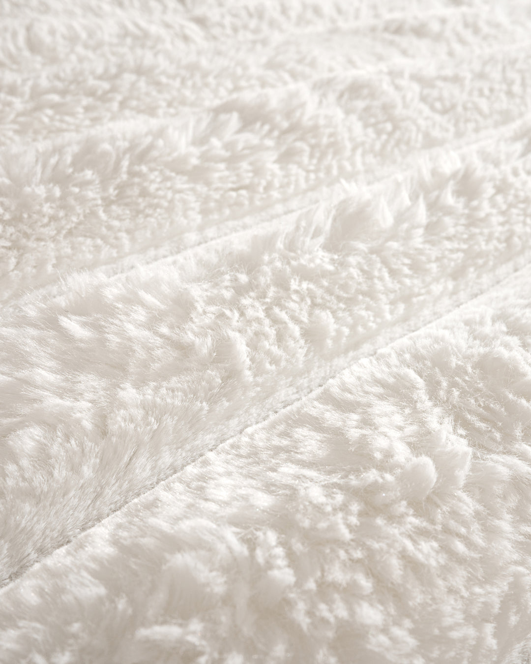 Close-up of the Cobertor Platinum Extra Suave Antártida by Intima Hogar, featuring soft, fluffy white faux fur with a wavy textured pattern and diagonal lines, giving it a cozy and plush appearance.