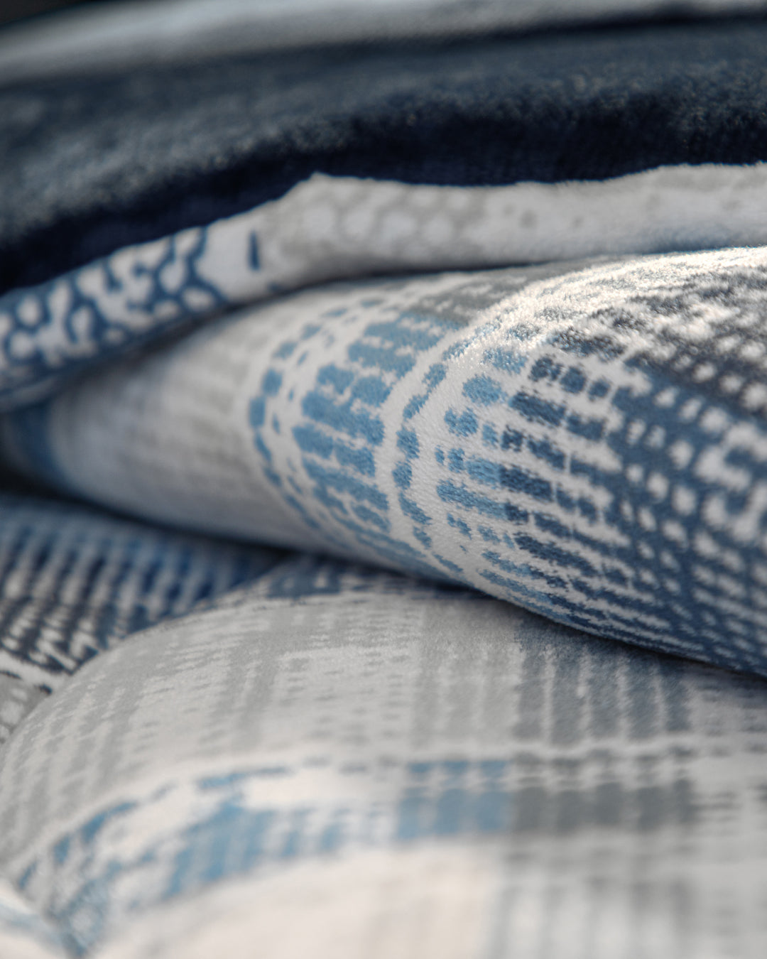 A close-up of the Intima Hogar Cobertor Flannel Extra Suave Duque, showcasing folded, patterned fabric in blue, gray, and white tones with a soft, textured surface and abstract designs. This modelo doble vista offers versatile style and cobertura cálida that feels suave al contacto.