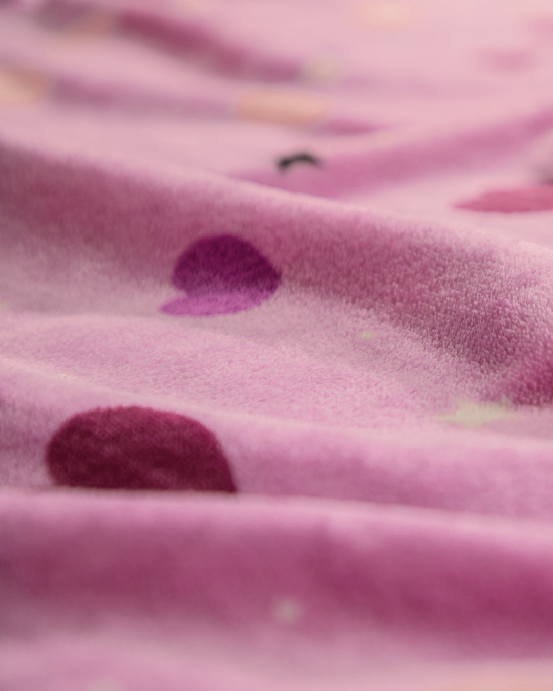 Close-up of the Cobertor Flannel Ligero Lilian by Intima Hogar, a soft pink fleece blanket featuring heart-shaped patterns in varying shades of pink and purple. The cozy fabric has a slightly wrinkled texture.