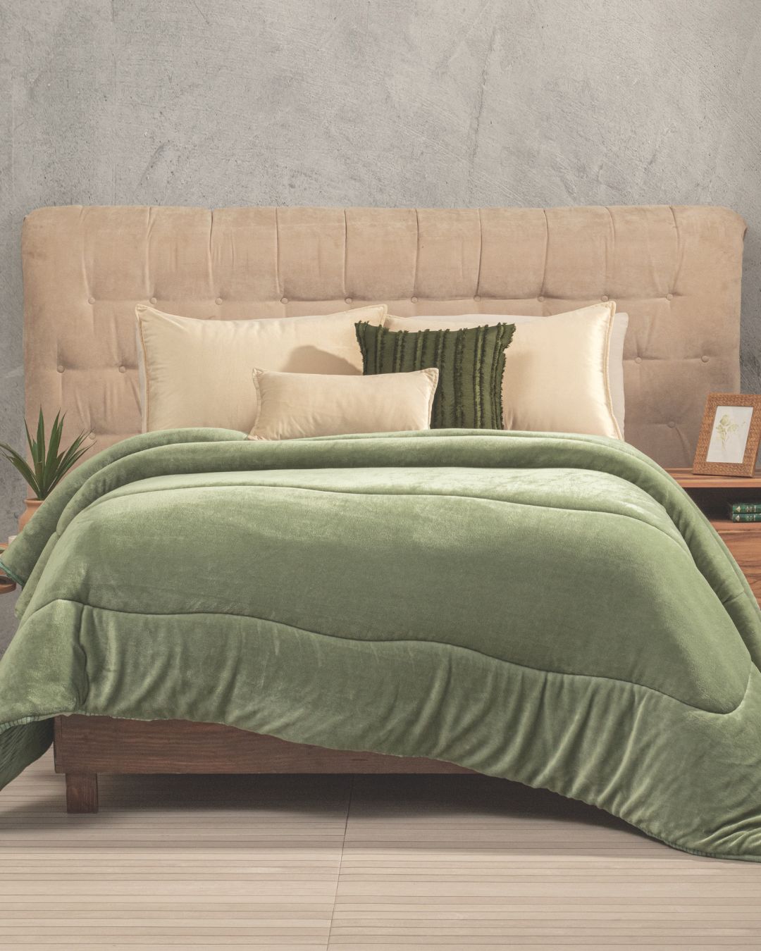 A neatly made bed with a beige tufted headboard, cream and green pillows, and the Cobertor Flannel Extra Suave Kioto by Intima Hogar in soft green with un acabado doble vista. Wooden nightstands with decor items and a small plant on either side evoke the tranquility of jardines japoneses.