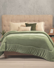 A neatly made bed with a beige tufted headboard, cream and green pillows, and the Cobertor Flannel Extra Suave Kioto by Intima Hogar in soft green with un acabado doble vista. Wooden nightstands with decor items and a small plant on either side evoke the tranquility of jardines japoneses.