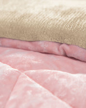 A close-up of the Cobertor Velvet Ice Deluxe Loto by Intima Hogar, showcasing its soft, textured layers with a beige top and a shiny, quilted pink fabric beneath.