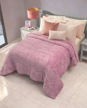 A neatly made bed in this dormitorio features the Cobertor Flannel Extra Suave Mónaco by Intima Hogar in pink, complemented by cream and pink pillows with patrones sutiles, and a pink lamp on a white nightstand. Sunlight streams through a window onto the tiled floor, enhancing the room’s suavidad.