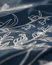 Close-up of white floral embroidery on a dark blue fabric from the Juego de Duvet Luxury Monarca by Intima Hogar, showing finely stitched flowers and leaves with a soft, textured appearance—ideal for adding an elegant touch to fundas decorativas or enhancing a classic edredón blanco.