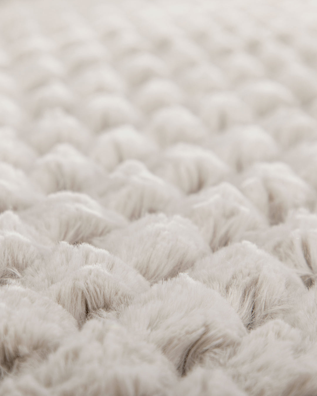 Close-up of the Cobertor Platinum Extra Suave Nickel by Intima Hogar, featuring a soft, textured, cream-colored surface with a quilted or tufted pattern. The raised, rounded sections evoke calidez suave through their plush fabric and gentle appearance.