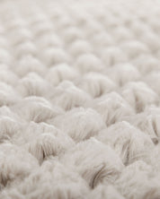 Close-up of the Cobertor Platinum Extra Suave Nickel by Intima Hogar, featuring a soft, textured, cream-colored surface with a quilted or tufted pattern. The raised, rounded sections evoke calidez suave through their plush fabric and gentle appearance.