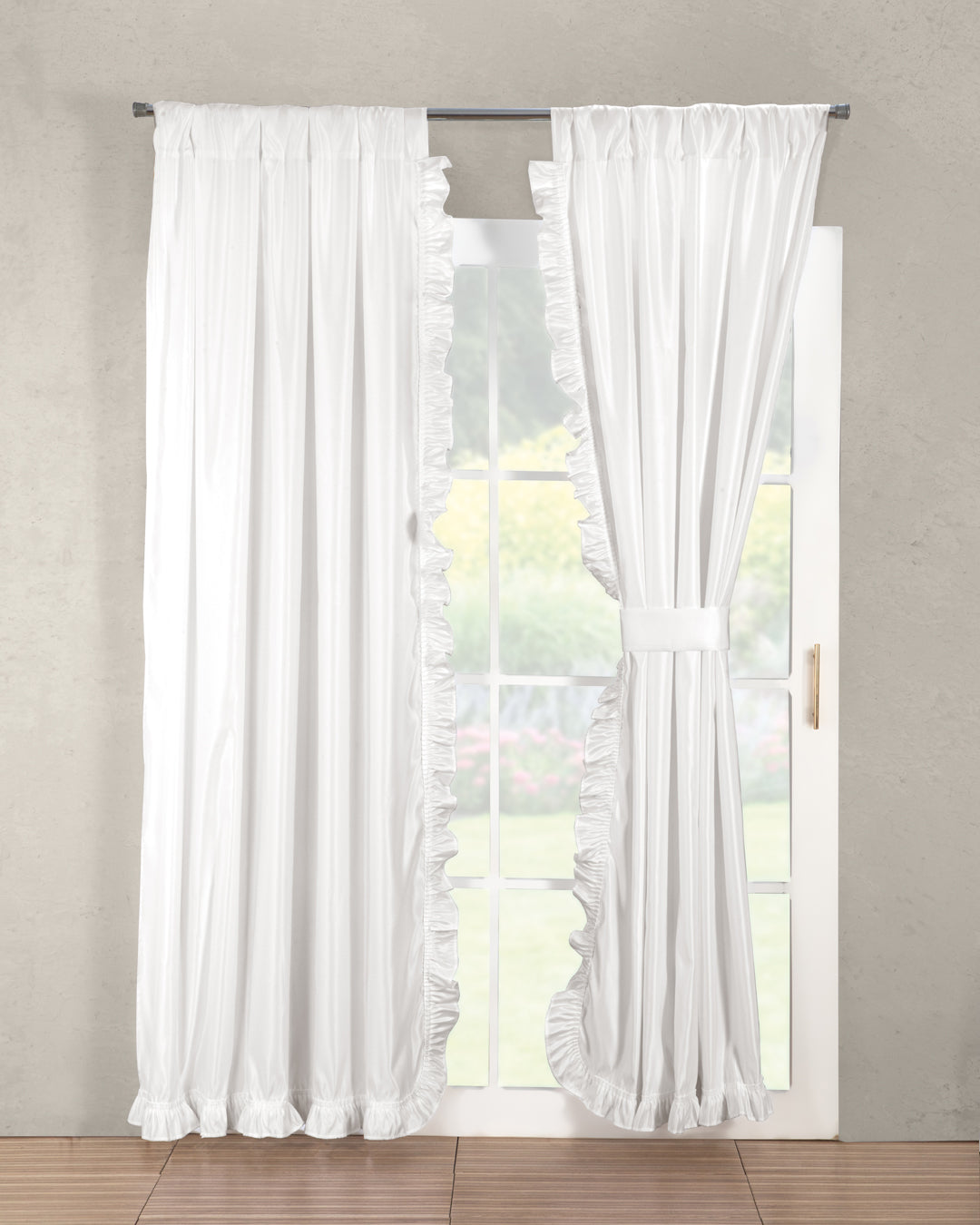 The Juego de Cortinas Paloma de Intima Hogar cuelga en una puerta de vidrio; una cortina está cerrada y la otra recogida a un lado, dejando ver el jardín desenfocado al exterior.