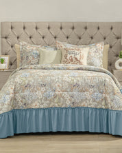 A neatly made bed with the Juego de Colcha Americana Porcelana by Intima Hogar and a light blue bed skirt brings a touch of descanso fresco to the dormitorio. Decorative pillows, including one with text, rest against a tufted beige headboard, while small plants and decor items on the bedside tables complete the inviting look.