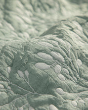 Close-up of the Juego de Edrecolcha Doble Vista Olmo by Intima Hogar, featuring light green quilted fabric with raised white embroidered leaf and branch patterns. The detailed stitching and soft texture make it perfect for a colcha or as fundas decorativas to enhance your cama’s look.