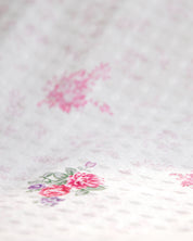 Un primer plano del Juego de Edredón Luxury Jardín de Intima Hogar muestra su suave tela blanca con un delicado estampado floral en tonos rosados, realzado por hojas verdes y pequeños detalles en morado. La textura ligeramente elevada crea un sutil efecto acolchado, perfecto para agregar encanto y comodidad a cualquier recámara, creando el ambiente ideal para un descanso reparador.