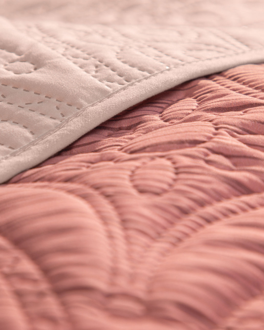 Close-up of the Juego de Edredón Ligero Carisma by Intima Hogar, featuring two quilted fabrics—one in off-white and one in dusty pink—with intricate stitched patterns. The white fabric is partially folded over the pink, highlighting the detailed textura capitonada and textured designs on both—perfect inspiration for edredones or fundas decorativas.