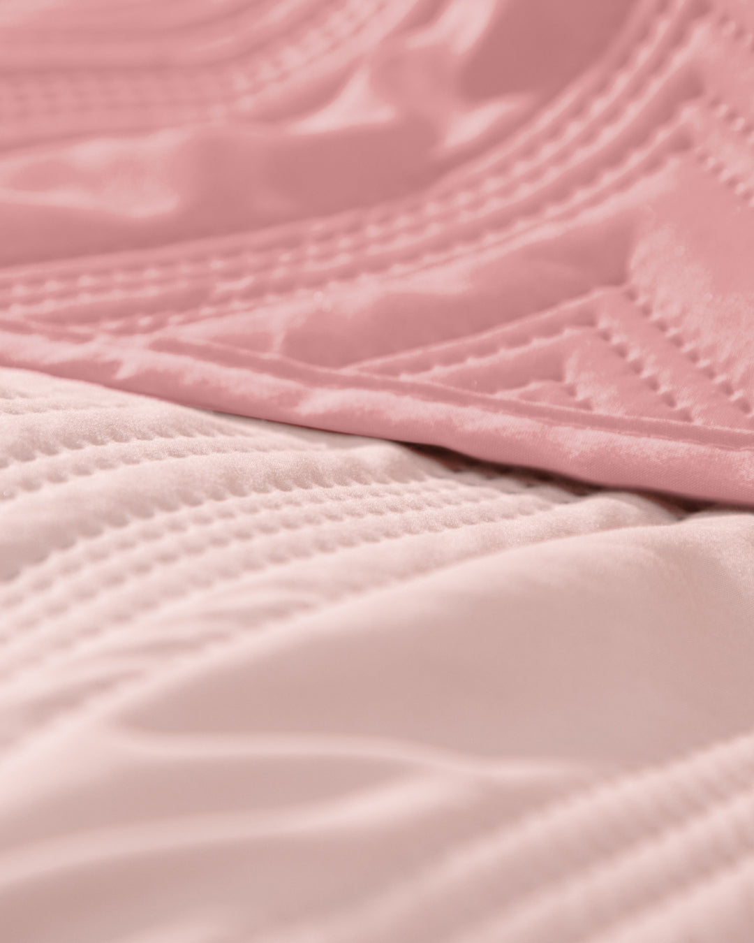 Close-up of the Juego de Edredón Ligero Mauve by Intima Hogar, featuring pink quilted fabric with stitched patterns and a soft texture—perfect as an edredón or funda decorativa for your cama. The image highlights the delicate folds and lines in the material.