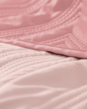 Close-up of the Juego de Edredón Ligero Mauve by Intima Hogar, featuring pink quilted fabric with stitched patterns and a soft texture—perfect as an edredón or funda decorativa for your cama. The image highlights the delicate folds and lines in the material.