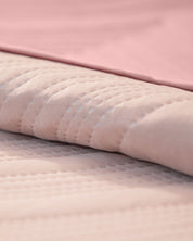 Close-up of the Juego de Edredón Ligero Mauve by Intima Hogar, featuring a soft, light mauve quilted design with a subtle textured pattern, lying beneath a smooth pink sheet on the bed.