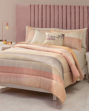 A neatly made bed features Intima Hogar’s Juego de Edredón Suave in soft peach, beige, and blush stripes, accompanied by matching pillows and crowned with a tall pink upholstered headboard—inviting you to enjoy un confort diario. The plush edredón from Intima Hogar promises a descanso reparador, while two white nightstands with lamps stand on either side.