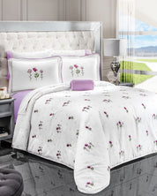 A neatly made bed features the Juego de Edredón Amore by Intima Hogar, with white comforter and pillowcases adorned with small purple flowers, set in a modern room with a tufted headboard and scenic window view.