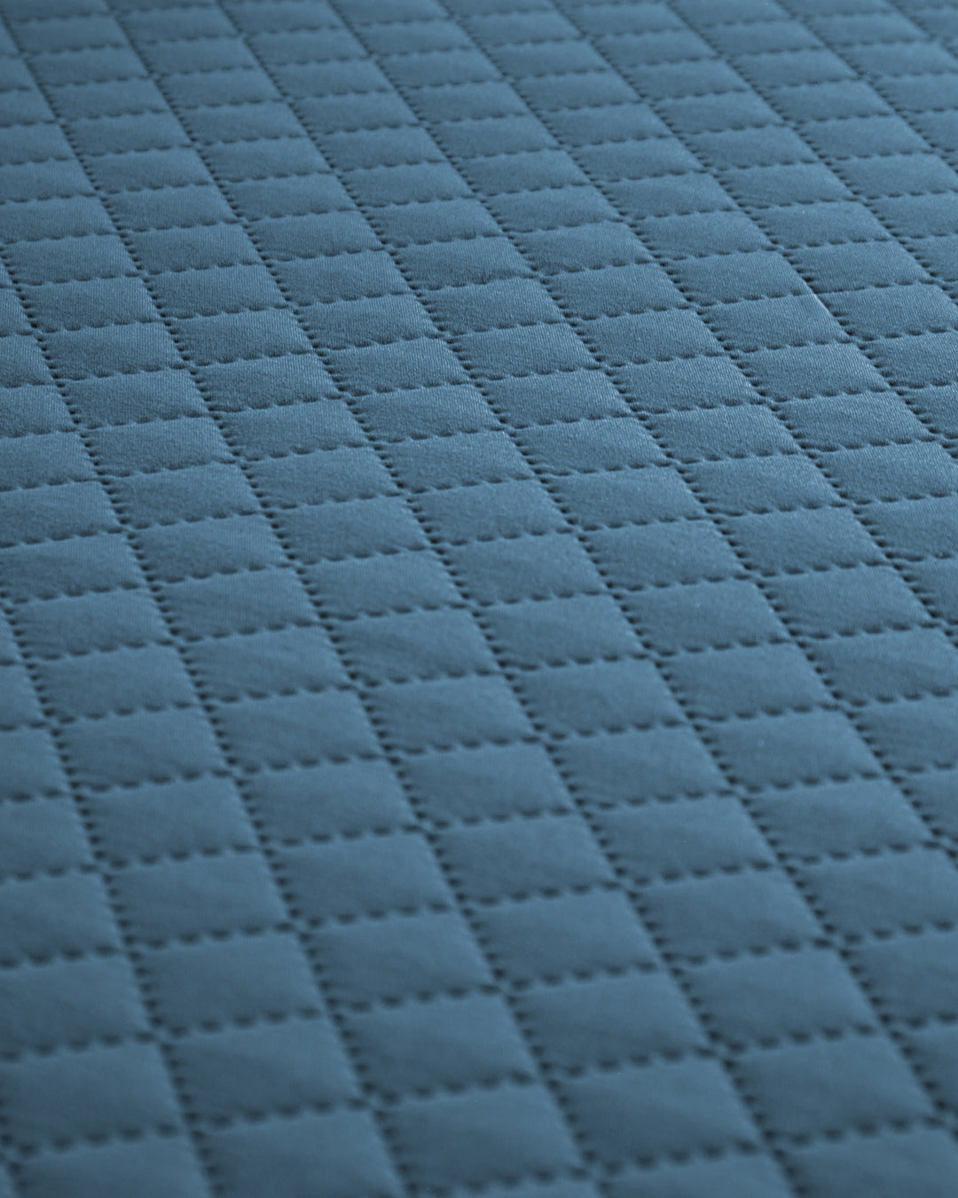 Close-up of the Juego de Edredón Edén by Intima Hogar, showing its blue fabric surface with a repeating square quilted pattern and stitched lines for a grid-like texture.