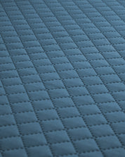 Close-up of the Juego de Edredón Edén by Intima Hogar, showing its blue fabric surface with a repeating square quilted pattern and stitched lines for a grid-like texture.