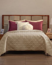 A bed dressed with the Juego de Edredón Ligero Burdeos from Intima Hogar, paired with burgundy and cream decorative shams and a round fluffy pillow. Wooden headboard, bedside tables with photos, and lamps create a cozy bedroom ambiance.