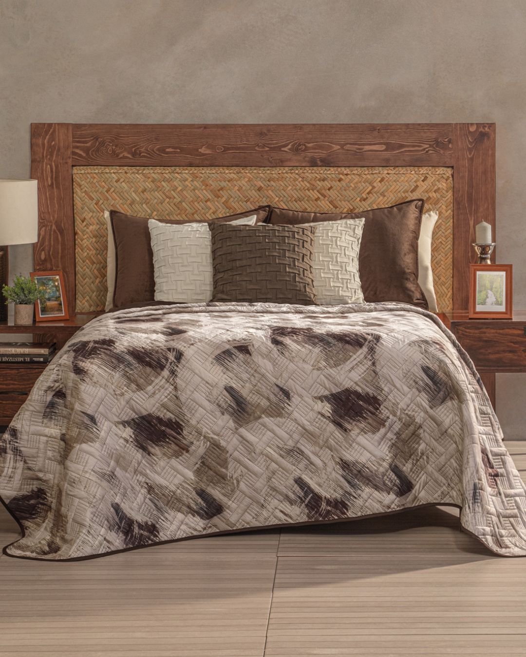 A neatly made bed with a wooden headboard showcases the Juego de Edredón Ligero Coffee by Intima Hogar in gray and brown, accented by decorative pillows. Nightstands with lamps, framed photos, and small plants complete this elegant habitación.