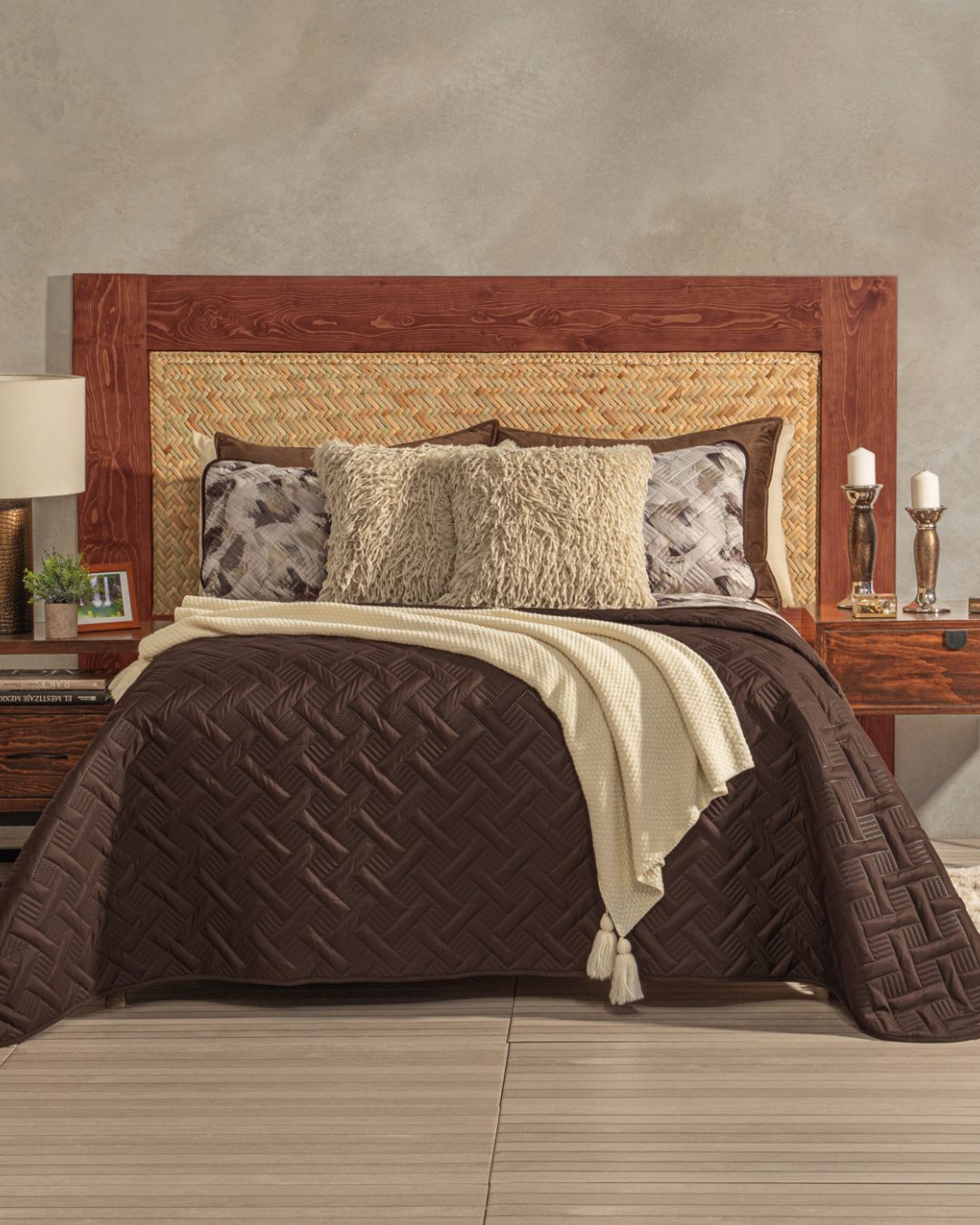 A cozy bed features the Intima Hogar Juego de Edredón Ligero Coffee, a large wooden and woven headboard, patterned pillows, cream throw, plus decorative lamps, books, and candles for a charming and elegante habitación.