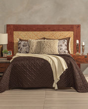 A cozy bed features the Intima Hogar Juego de Edredón Ligero Coffee, a large wooden and woven headboard, patterned pillows, cream throw, plus decorative lamps, books, and candles for a charming and elegante habitación.