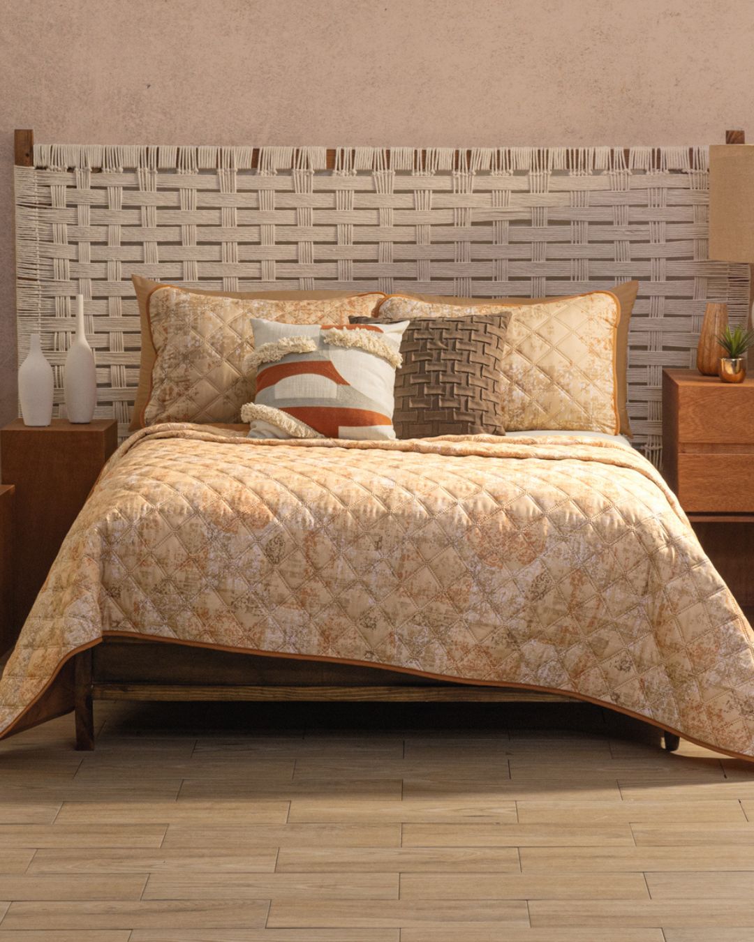 A cozy dormitorio contemporáneo with a woven headboard and bed dressed in the Juego de Edredón Ligero Destello by Intima Hogar, plus decorative pillows. Two wooden nightstands with lamps flank the bed over a light tile floor.