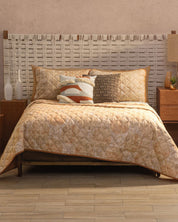 A cozy dormitorio contemporáneo with a woven headboard and bed dressed in the Juego de Edredón Ligero Destello by Intima Hogar, plus decorative pillows. Two wooden nightstands with lamps flank the bed over a light tile floor.