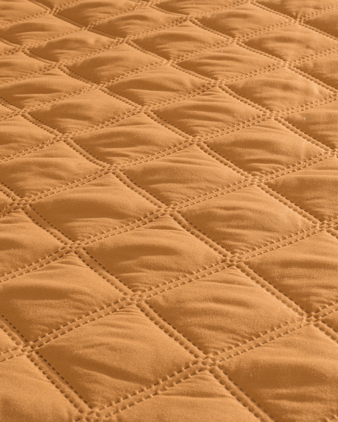 Close-up of the Juego de Edredón Ligero Destello by Intima Hogar, featuring quilted fabric with a diamond pattern in warm tan. Visible stitching outlines each diamond, giving it a textured and padded look.