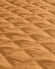Close-up of the Juego de Edredón Ligero Destello by Intima Hogar, featuring quilted fabric with a diamond pattern in warm tan. Visible stitching outlines each diamond, giving it a textured and padded look.