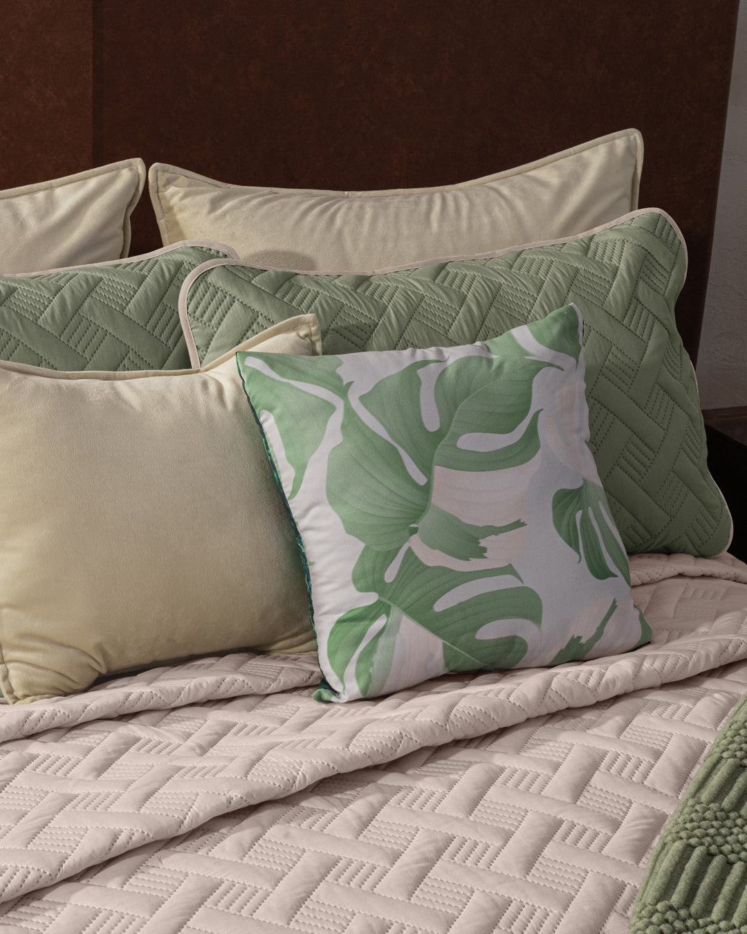 The Juego de Edredón Ligero Esperanza de Intima Hogar viste la cama con elegancia y calidez, combinando almohadas beige y verdes, una con patrón de hojas verdes, y un edredón beige acolchado para crear un ambiente acogedor.