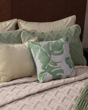 The Juego de Edredón Ligero Esperanza de Intima Hogar viste la cama con elegancia y calidez, combinando almohadas beige y verdes, una con patrón de hojas verdes, y un edredón beige acolchado para crear un ambiente acogedor.