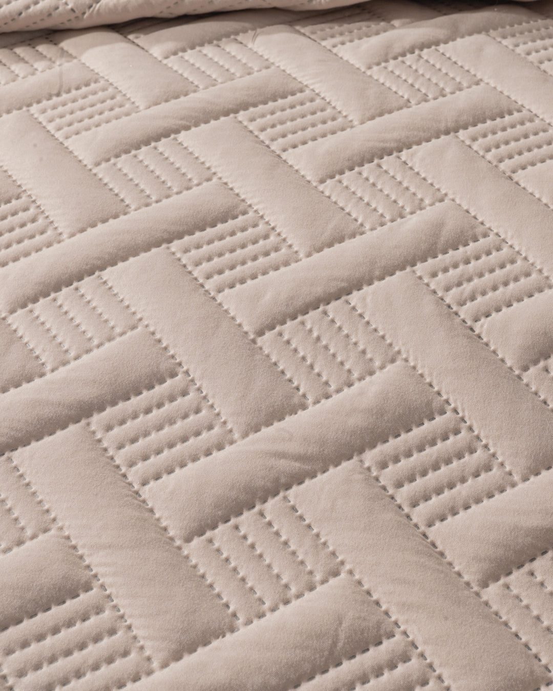 Close-up of the Juego de Edredón Ligero Esperanza by Intima Hogar, showcasing its quilted beige fabric with a herringbone pattern and stitched lines for a textured, structured look.