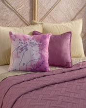 Two decorative throw pillows—one with pink abstract line art and one solid mauve—rest on a beige bed dressed in the Juego de Edredón Ligero Espíritu quilt by Intima Hogar, with beige pillows in the background.